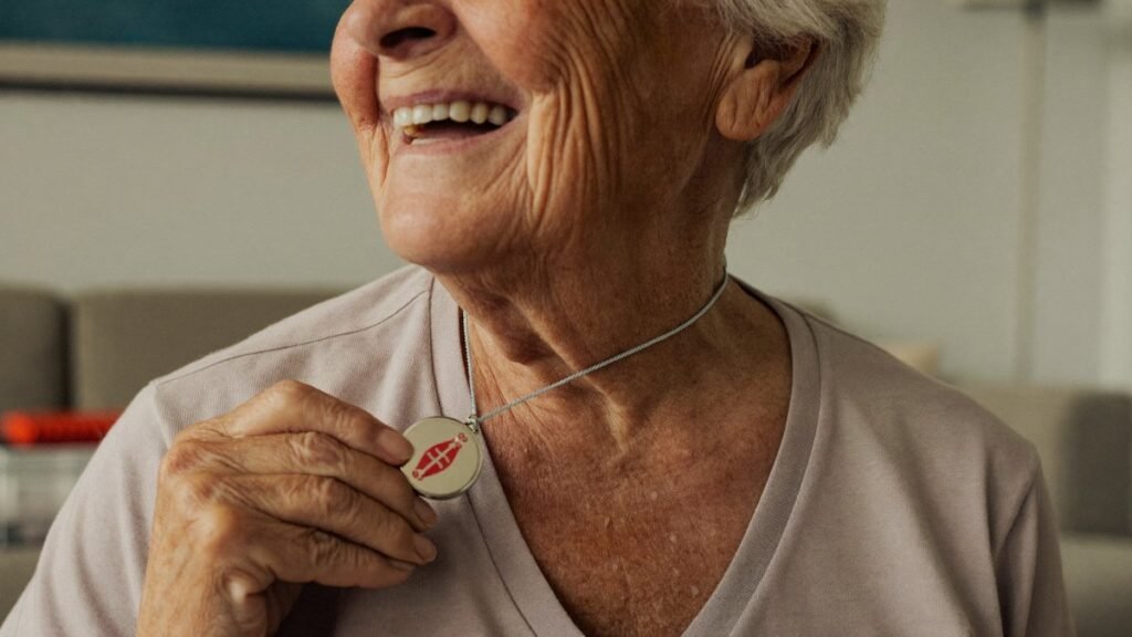 Femme âgée souriante portant un médaillon de téléalarme chez elle
